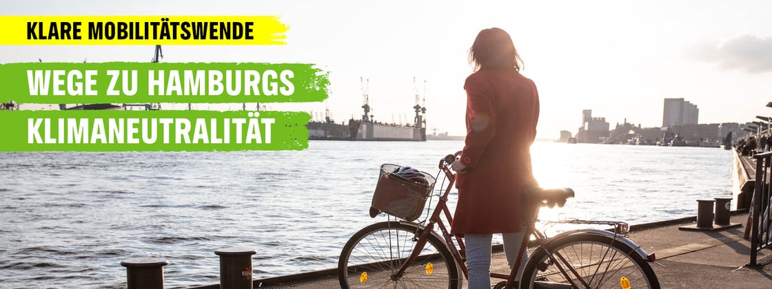 Frau mit Fahrrad schaut an den Hamburger Landungsbrücken auf die Elbe.